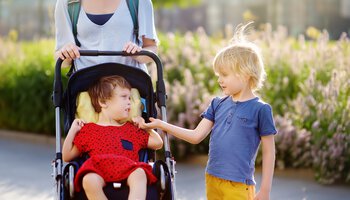 Kleiner Junge und ein behindertes Kind im Kinderwagen halten sich an der Hand | © adobestock_maria-sbytova_274645887
